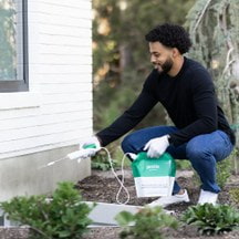 Man spraying Pestie on foundation of house.